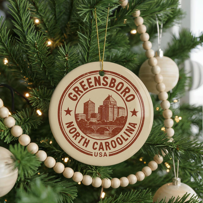 A Christmas tree decorated with ornaments, including a circular ornament with the text "GREENSBORO NORTH CAROLINA USA" printed on it.