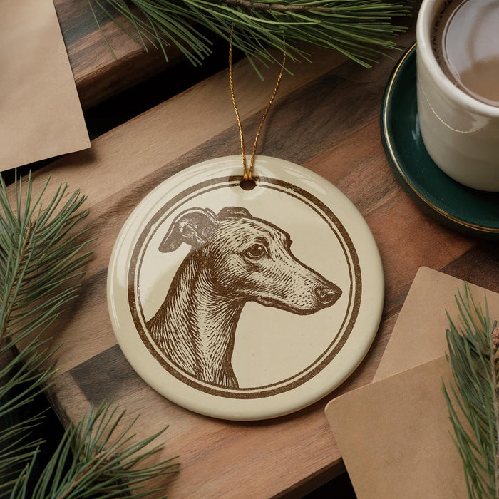 a ceramic ornament with a detailed illustration of a dog's head, placed on a wooden surface. The ornament is surrounded by pine branches and a cup of coffee, creating a cozy and festive atmosphere.
