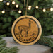 A round ornament with a graphic of a llama and the word "GUANACO" on it, hanging from a string.