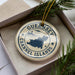 A circular ornament with the text "GUERNSEY CHANNEL ISLANDS" printed on it, surrounded by pine branches.