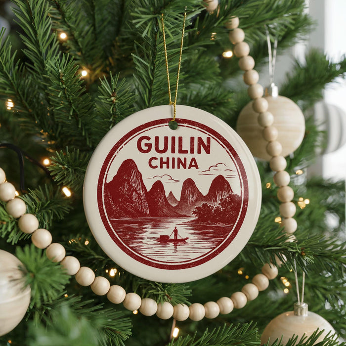 A Christmas tree decorated with ornaments, including a circular ornament with a red and white design that says "GUILIN CHINA" and a boat illustration.