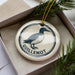 A ceramic ornament in a box, featuring a graphic of a bird and the word "GUILLLEMOT" written on it.