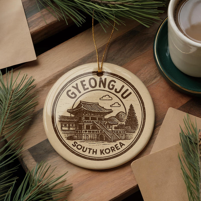A decorative ornament featuring a traditional Korean temple, with the text "GYEONGJU SOUTH KOREA" printed on it, is displayed on a wooden surface alongside a cup of coffee and some pine branches.