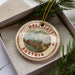 A circular ornament with the text "HALLSTATT AUSTRIA" and an illustration of a town, surrounded by greenery.