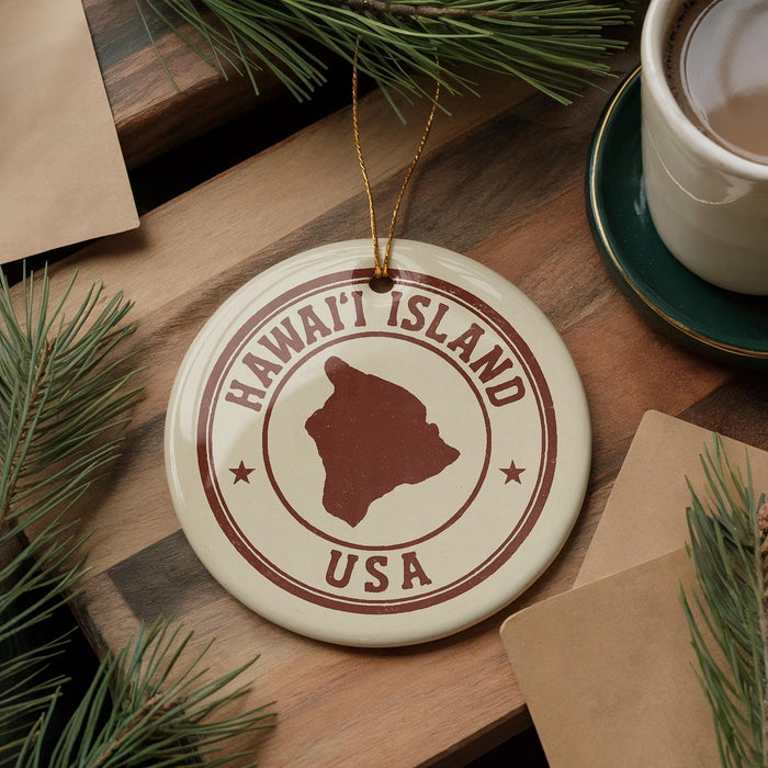 A circular ornament with the text "HAWAII'I ISLAND USA" printed on it, surrounded by pine branches and a cup of coffee on a wooden surface.