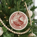 A Christmas tree decorated with ornaments, including a circular ornament with the text "HAWAII'I VOLCANOES NATIONAL PARK" and a wooden bead decoration.