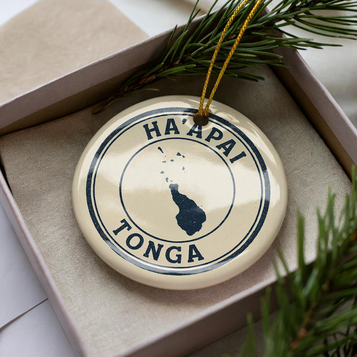 A circular ornament with the text "HA APAI TONGA" printed on it, surrounded by pine branches.