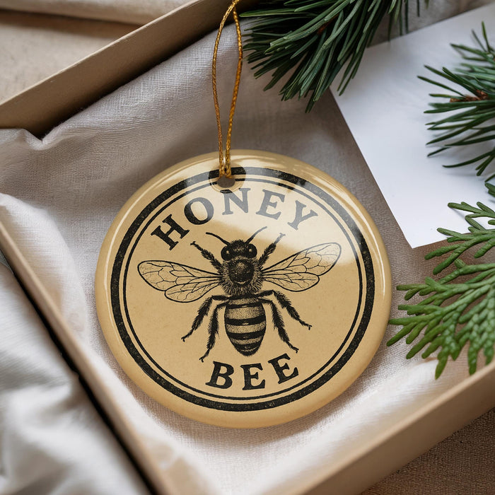 A round ornament with a bee image and the text "HONEY BEE" is displayed in a box with pine branches.