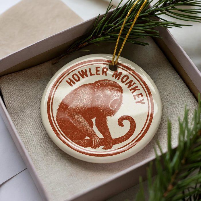 A round ornament with a monkey image and the text "HOWLER MONKEY" on it, placed in a box with pine branches.