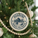 A Christmas tree decorated with ornaments, including a circular ornament with the text "HUAHINE FRENCH POLYNESIA" and a sailboat illustration.