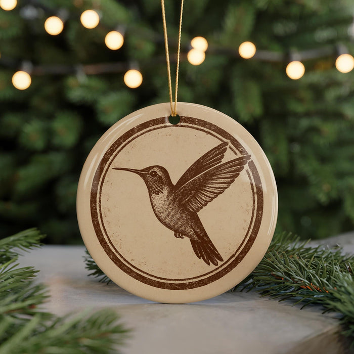 A round ornament featuring a hummingbird is displayed in front of a blurred background of Christmas lights.