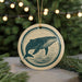 A round ornament featuring a whale design is displayed in front of a blurred background with Christmas lights.