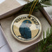 A ceramic ornament in a box, featuring a blue parrot with a yellow beak.