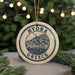 A round ornament with the text "HYDRA GREECE" and an illustration of a town or village, hanging from a string.