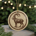 A round ornament featuring a goat with a curved horn, placed on a surface with pine branches in the background.