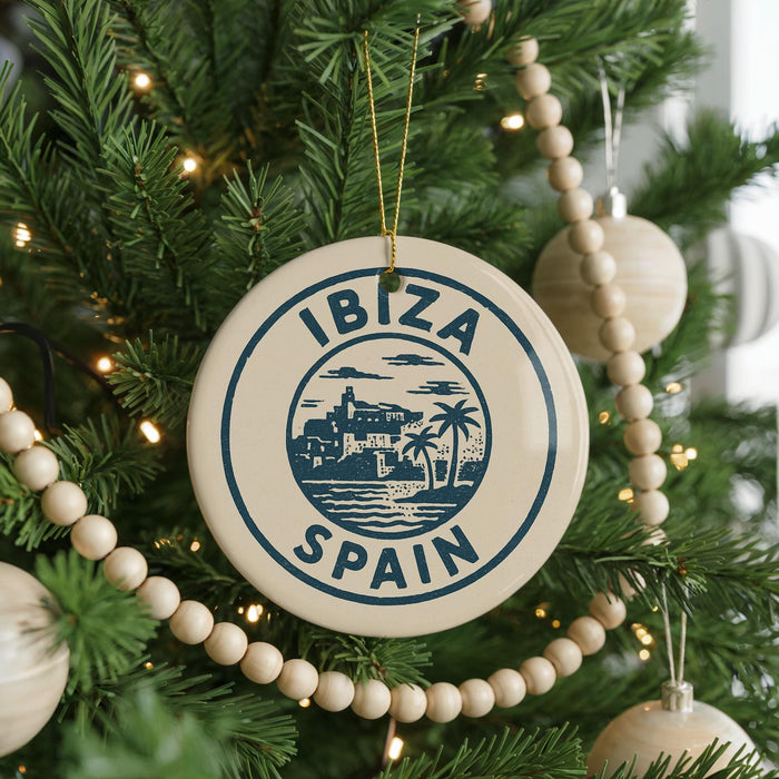 A Christmas tree decorated with a circular ornament that says "IBiza Spain" and features a graphic of a coastal town with palm trees.