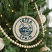 A Christmas tree decorated with a circular ornament that says "IBiza Spain" and features a graphic of a coastal town with palm trees.