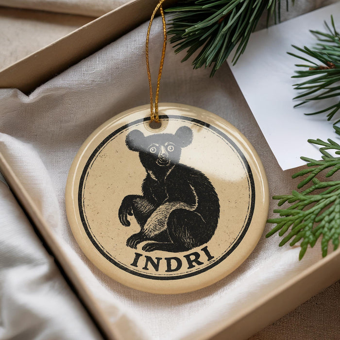 A circular ornament with a bear image and the word "INDRI" printed on it, placed on a surface with pine branches and a white paper.