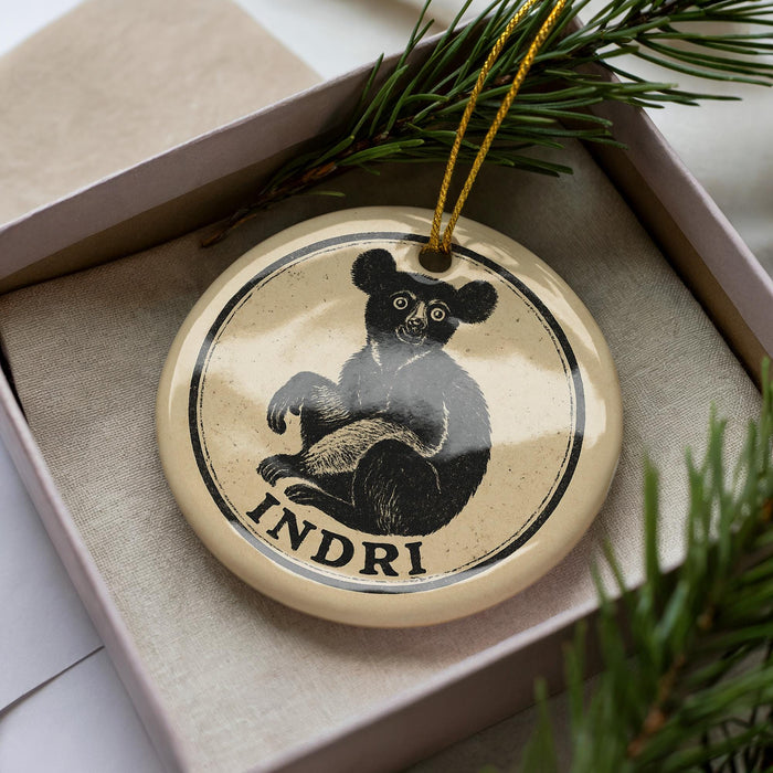 A circular ornament with a black bear image and the word "INDRI" written on it, placed inside a box with pine branches.