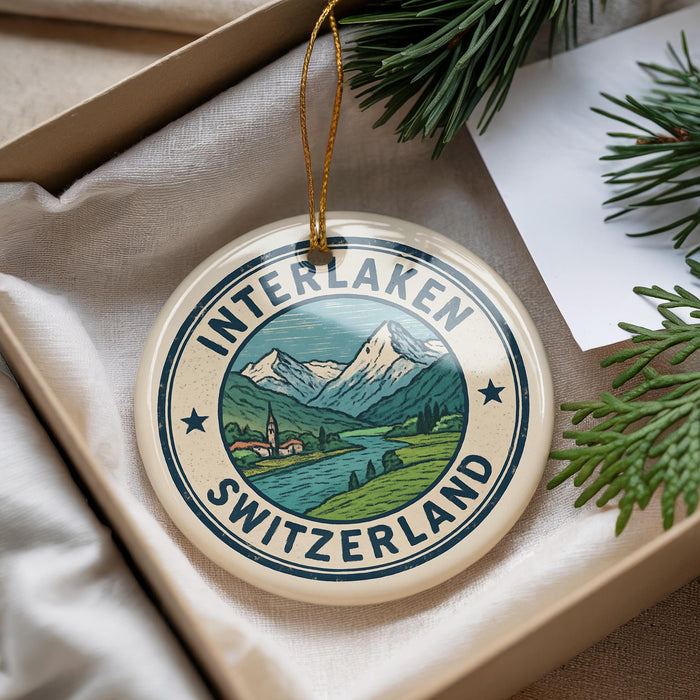 A decorative ornament with a mountain landscape and Swiss flag design, placed in a box with pine branches.