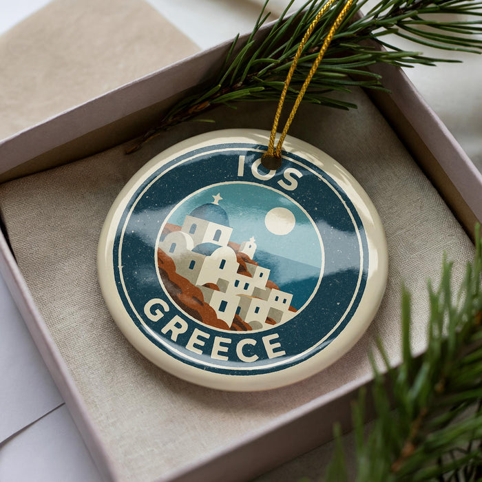 A circular ornament with a design of a Greek island and buildings, surrounded by greenery and a string.
