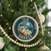 A circular ornament on a Christmas tree, featuring a design of a Greek island with a church and a full moon.
