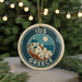 A circular ornament with a design of a Greek island and the text "IOS GREECE" is displayed in front of a Christmas tree with twinkling lights.