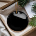A black circular ornament is displayed in a box, surrounded by pine branches and a white card.
