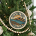 A round ornament on a Christmas tree, featuring a scenic image of the island of Bolivia.