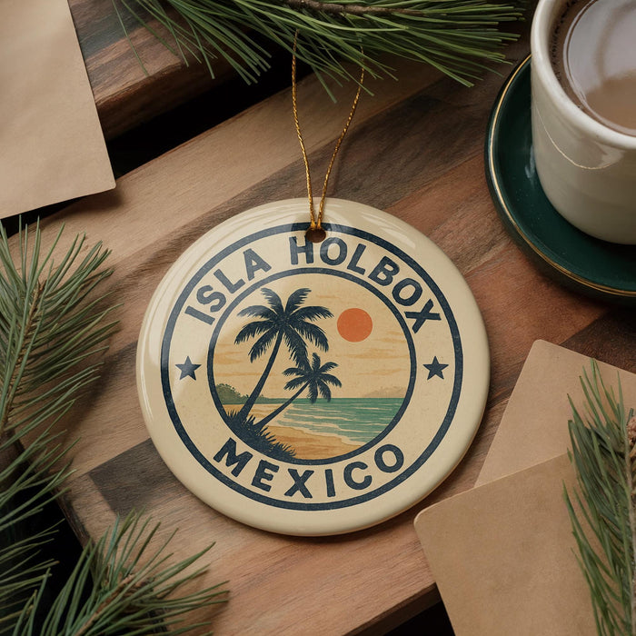 A circular ornament with the text "ISLA HOLBOX MEXICO" and a palm tree design, hanging on a wooden surface next to a cup of coffee and some pine branches.