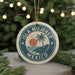 A circular ornament with the text "ISLA MUJERES MEXICO" and a palm tree design, hanging from a string against a background of Christmas lights and greenery.