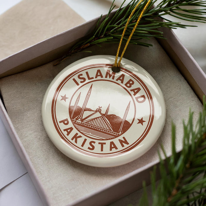 A circular ornament with the text "ISLAMABAD PAKISTAN" printed on it, surrounded by pine branches.