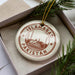A circular ornament with the text "ISLAMABAD PAKISTAN" printed on it, surrounded by pine branches.