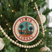 A circular ornament on a Christmas tree, featuring a red and white border and a picture of a tower surrounded by palm trees.
