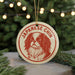 A round ornament with a red and white design featuring a dog's face, hanging from a string.