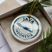 A circular ornament with the text "JAMAICA INDONESIA" printed on it, surrounded by pine branches.