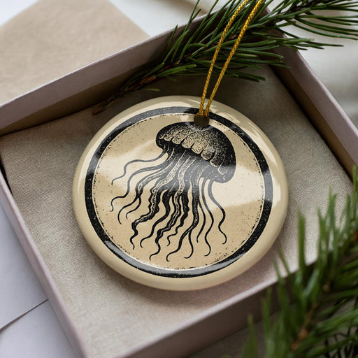 A round ornament with a black and white illustration of a jellyfish is displayed in a box, surrounded by pine branches.