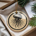 A round ornament with a black and white illustration of a jellyfish is displayed in a box, surrounded by pine branches.