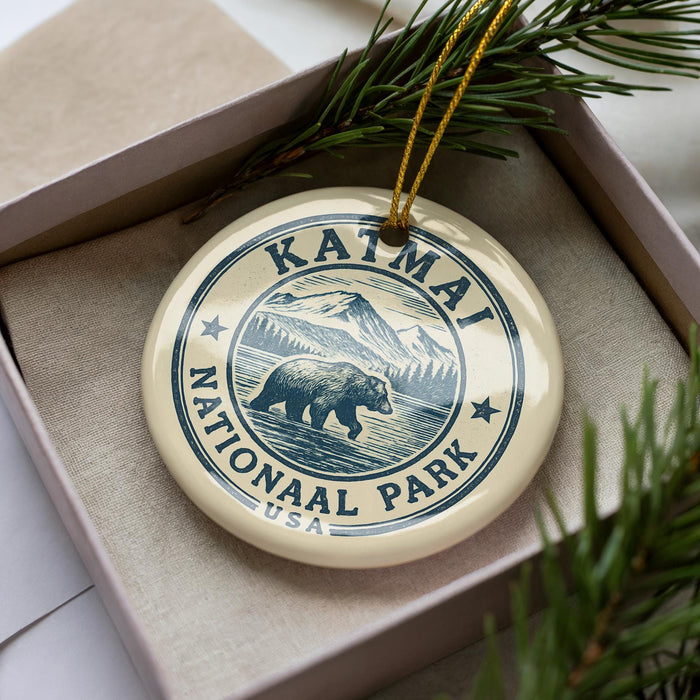A circular ornament with the text "KAIMAI NATIONAL PARK USA" printed on it, featuring a bear illustration. The ornament is placed inside a box with pine branches.