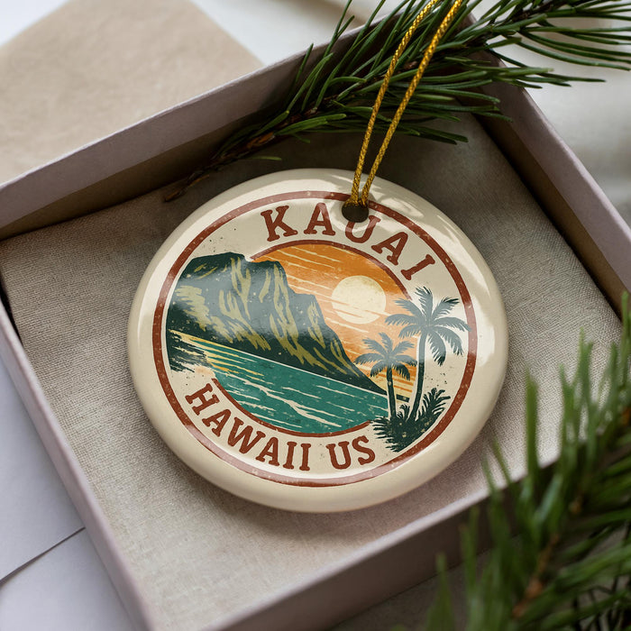 A circular ornament with a tropical island landscape and palm trees, featuring the text "Kauai Hawaii Us" on it, is displayed in a box with pine branches.