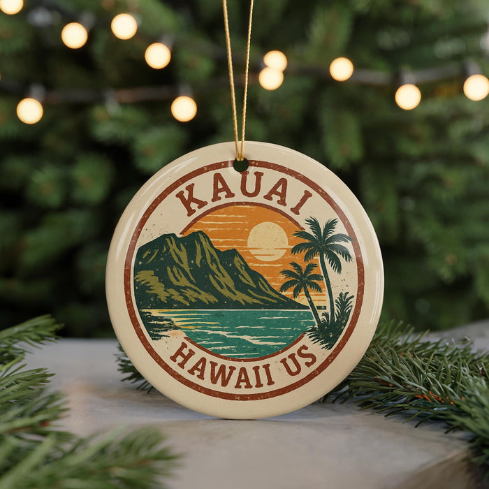 A circular ornament with the text "Kauai Hawaii Us" and a graphic of a tropical landscape, including a mountain, palm trees, and a sunset, is hanging from a string.