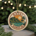 A circular ornament with the text "Kauai Hawaii Us" and a graphic of a tropical landscape, including a mountain, palm trees, and a sunset, is hanging from a string.
