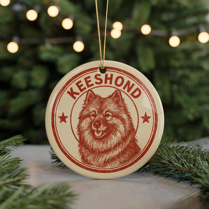 A red and white circular ornament with a picture of a dog's face and the name "Keeshond" printed on it, hanging from a string.