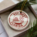 A circular ornament with the text "KEY WEST FLORIDA USA" printed on it, placed inside a box with pine branches.