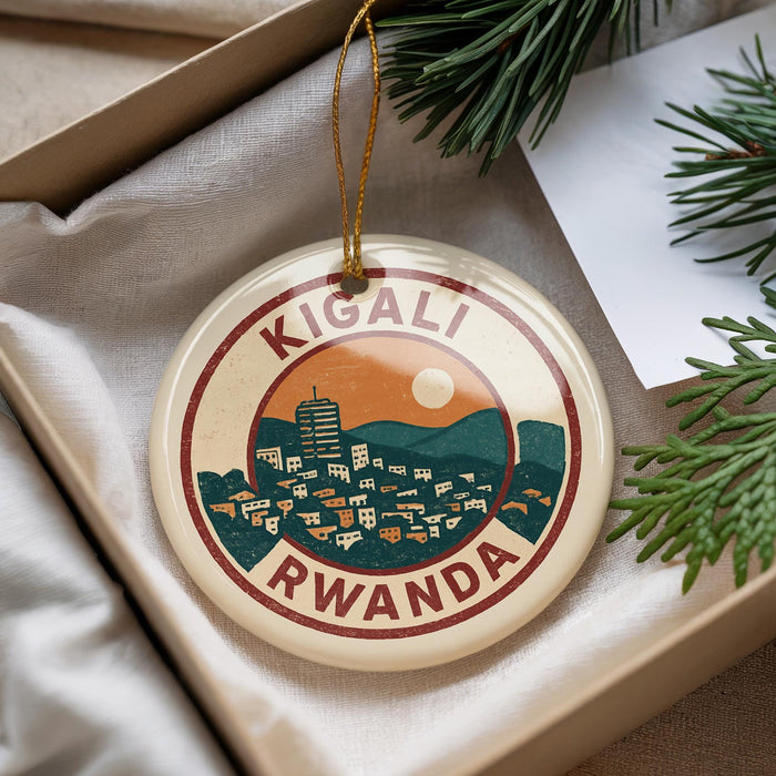 A decorative ornament with the text "KIGALI RWANDA" and an illustration of a cityscape with mountains, hanging from a string.