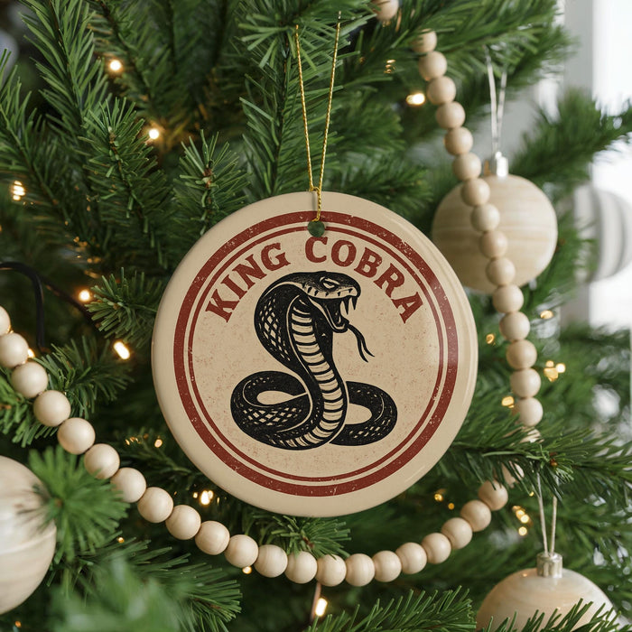 A Christmas tree decorated with ornaments, including a round ornament with a red and white design featuring a black and white illustration of a cobra and the text "KING COBRA".