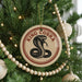 A Christmas tree decorated with ornaments, including a round ornament with a red and white design featuring a black and white illustration of a cobra and the text "KING COBRA".