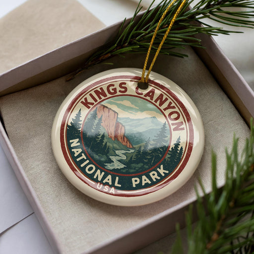 A decorative ornament in the shape of the Kings Canyon National Park logo, featuring a mountain landscape and pine trees, is displayed in a box with pine branches.