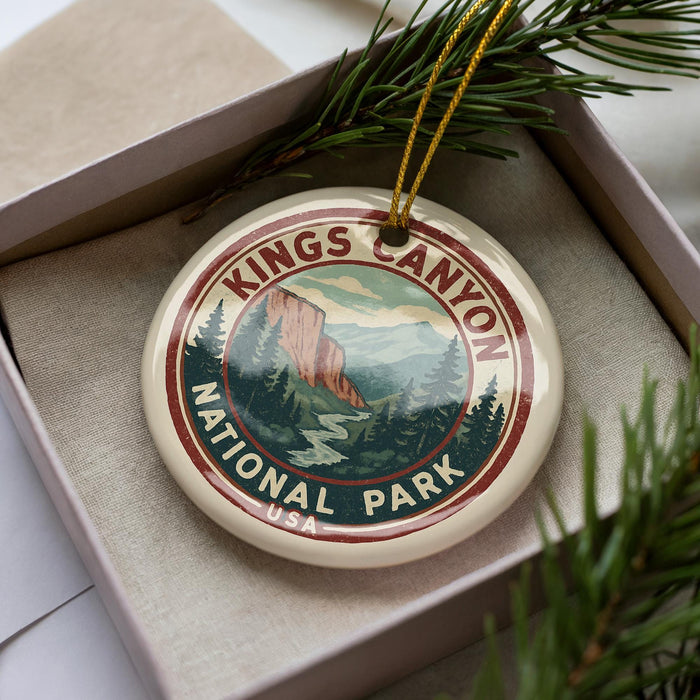 A decorative ornament in the shape of the Kings Canyon National Park logo, featuring a mountain landscape and pine trees, is displayed in a box with pine branches.