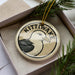 A decorative ornament in a box, featuring a bird design with the text "KITTIWAKE" on it.
